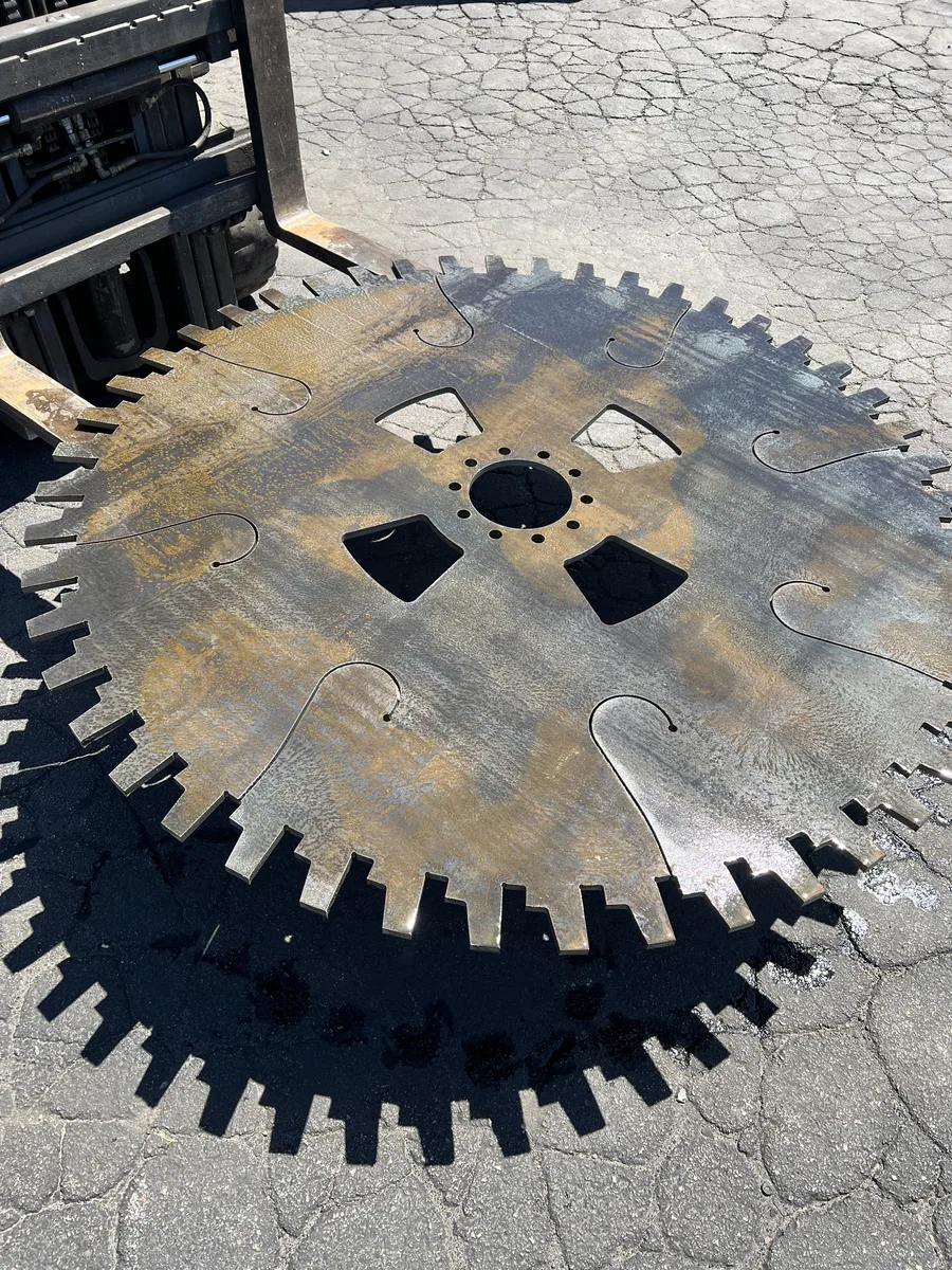 Large waterjet-cut steel industrial gear with toothed edge and internal cutouts