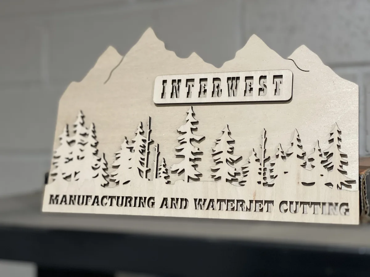 Laser-cut wood Interwest Manufacturing sign with mountain and tree scene